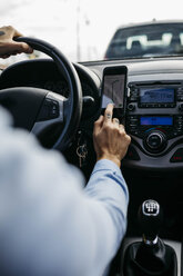 Close-up of man with tattooed hand driving car using cell phone as navigation system - JRFF02542