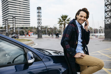 Spain, Barcelona, smiling man on cell phone outside car in the city - JRFF02545