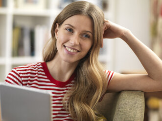 Smiling young woman relaxing at home using a tablet - ABRF00278