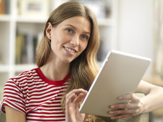 Lächelnde junge Frau, die sich zu Hause mit einem Tablet entspannt - ABRF00279