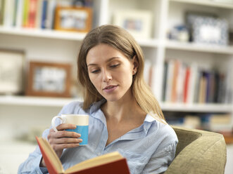 Junge Frau mit einem heißen Getränk, die sich zu Hause beim Lesen eines Buches entspannt - ABRF00282