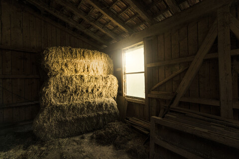 Traditionelle Bauernscheune mit Strohballen und Lichteinfall durch ein Fenster, lizenzfreies Stockfoto
