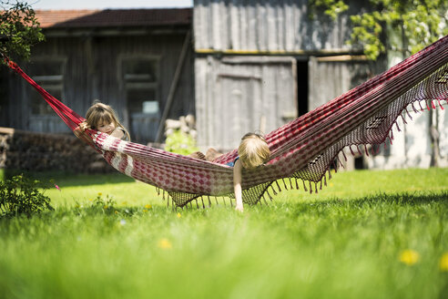 Zwei Kinder entspannen sich in einer Hängematte im Garten eines Bauernhofs - SBOF01698