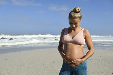 Aktive schwangere Frau am Strand, die ihren Bauch berührt - ECPF00333