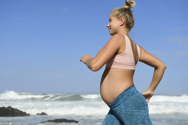 Lächelnde schwangere Frau beim Joggen am Strand - ECPF00342