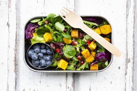 Gemischter Salat mit gebratenem Tofu, Rotkohl, Granatapfelkernen, Heidelbeeren und Kurkuma in der Lunchbox, lizenzfreies Stockfoto