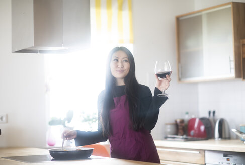 Junge Frau kocht zu Hause und hält ein Glas Rotwein in der Hand - SGF02226