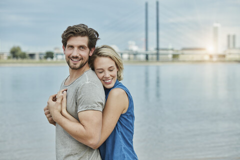 Glückliches junges Paar, das sich am Flussufer umarmt, lizenzfreies Stockfoto