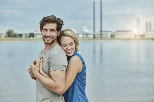 Glückliches junges Paar, das sich am Flussufer umarmt - RORF01672