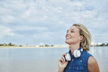 Germany, Duesseldorf, happy young woman with headphones at Rhine riverbank - RORF01683