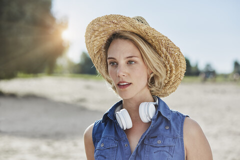 Portrait of young woman with headphones and straw hat on the beach stock photo