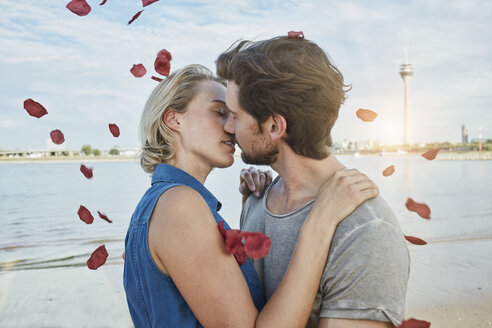 Deutschland, Düsseldorf, verliebtes junges Paar küsst sich am Rheinufer, umgeben von fallenden Rosenblättern - RORF01691