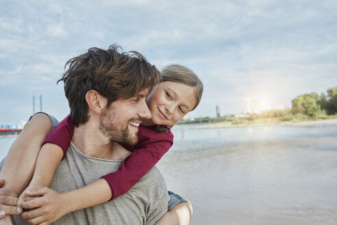 Germany, Duesseldorf, happy father carrying daughter piggyback at Rhine riverbank - RORF01702