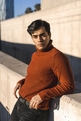 Portrait of fashionable young man wearing turtleneck pullover leaning on a wall at sunlight - AFVF02303