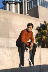 Portrait of fashionable young man wearing turtleneck pullover sitting on a wall at sunlight - AFVF02306