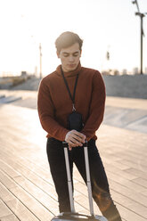 Portrait of young fashionable man with luggage standing at backlight - AFVF02307