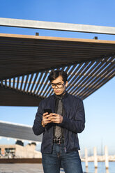 Portrait of fashionable young businessman wearing glasses and tie looking at cell phone - AFVF02315