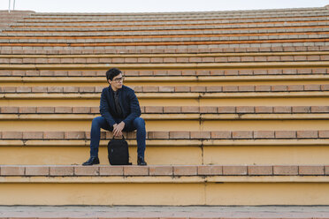 Junger Geschäftsmann mit Rucksack sitzt auf einer Treppe und schaut in die Ferne - AFVF02327