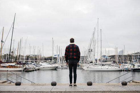 Rückenansicht eines jungen Mannes in Freizeitkleidung mit Blick auf den Hafen - JRFF02555