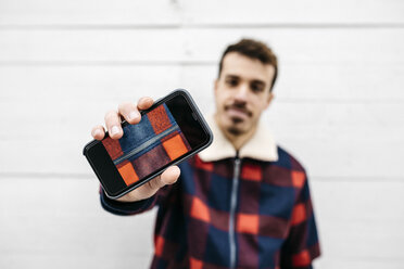 Junger Mann zeigt ein Foto auf dem Handy in den Farben seiner Jacke - JRFF02565
