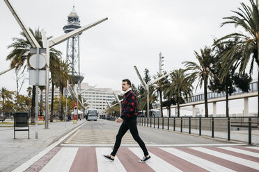 Young man with casual clothes walking on pedestrian crossing in Barcelona - JRFF02573