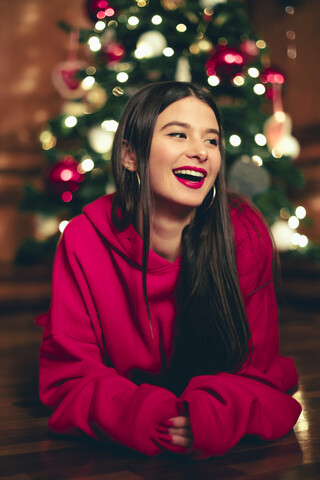 Porträt eines lachenden Teenagers, der vor einem Weihnachtsbaum auf dem Boden liegt, lizenzfreies Stockfoto