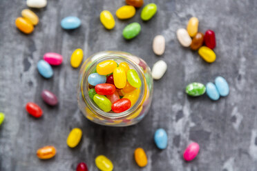 Glass of colourful sweet jellybeans on gray background - SARF04084