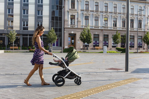 Mother pushing baby in a stroller in the city - MOMF00613