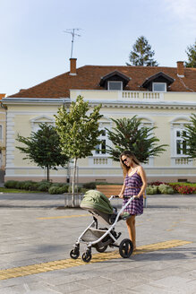 Mutter mit Baby in einem Kinderwagen in der Stadt - MOMF00617