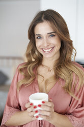 Porträt einer lächelnden jungen Frau im Morgenmantel, die eine Tasse Kaffee hält - PNEF01254