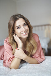 Portrait of smiling young woman in dressing gown lying in bed - PNEF01266