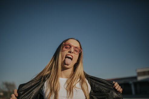 Porträt einer jungen Frau im Freien, die ihre Zunge herausstreckt - DMGF00003