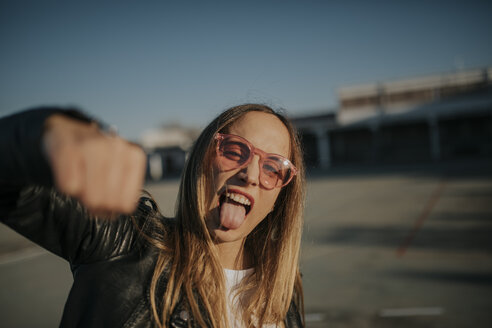 Portrait of young woman outdoors sticking out tongue and punching - DMGF00004