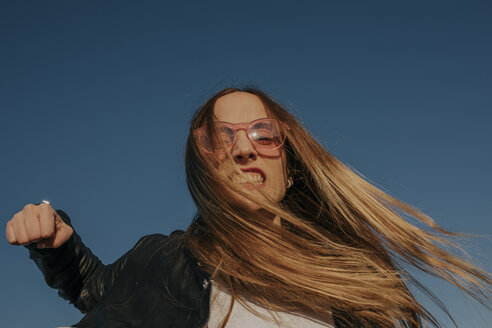 Portrait of aggressive young woman punching under blue sky - DMGF00005