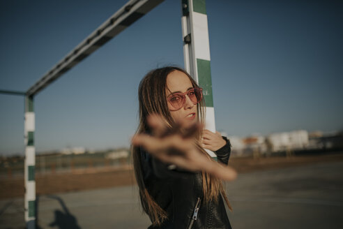 Porträt einer jungen Frau mit Sonnenbrille auf einem Sportplatz, die ihre Hand ausstreckt - DMGF00007