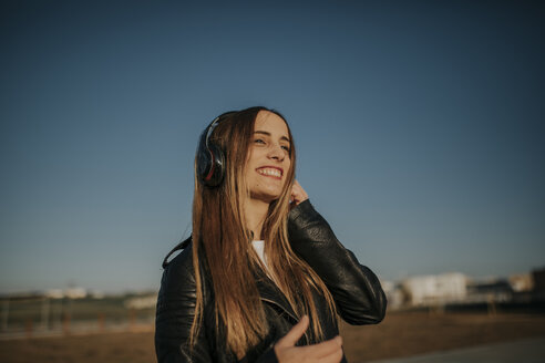 Glückliche junge Frau hört Musik mit Kopfhörern im Freien - DMGF00013