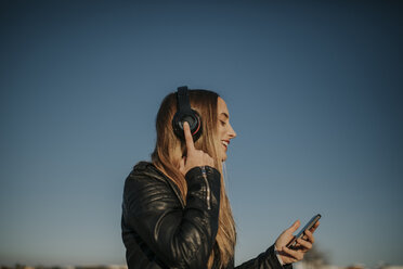 Glückliche junge Frau hört Musik mit Kopfhörern im Freien - DMGF00019