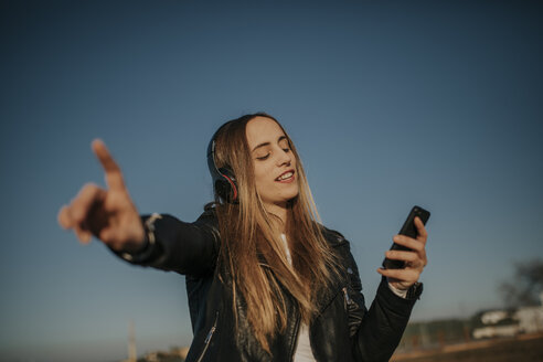 Glückliche junge Frau hört Musik mit Kopfhörern im Freien - DMGF00020