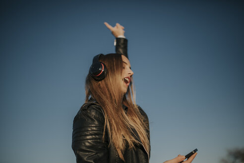 Glückliche junge Frau hört Musik mit Kopfhörern im Freien - DMGF00021