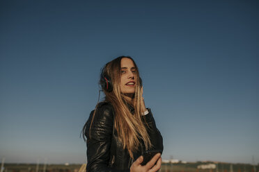 Smiling young woman listening music with headphones outdoors - DMGF00022