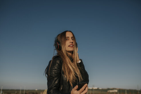 Lächelnde junge Frau hört Musik mit Kopfhörern im Freien - DMGF00022