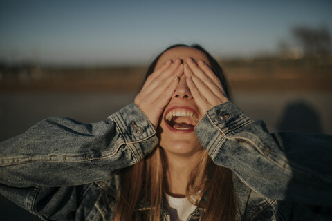 Fröhliche junge Frau, die ihre Augen im Freien bedeckt, lizenzfreies Stockfoto