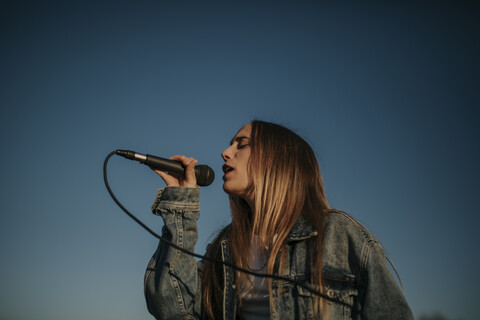 Young woman singing with a microphone under blue sky stock photo