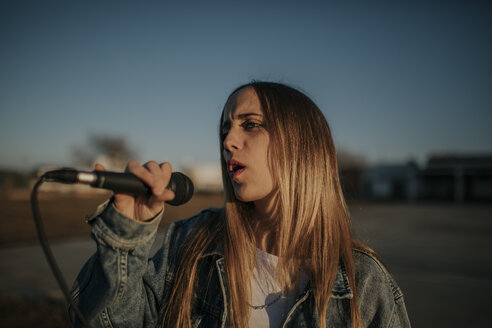Junge Frau singt mit einem Mikrofon im Freien - DMGF00037