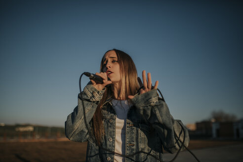Junge Frau singt mit einem Mikrofon im Freien - DMGF00038