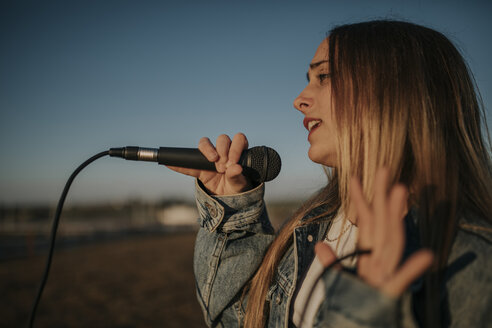 Junge Frau singt mit einem Mikrofon im Freien - DMGF00039