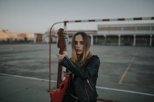 Porträt einer coolen jungen Frau mit Gitarre auf einem Sportplatz - DMGF00051