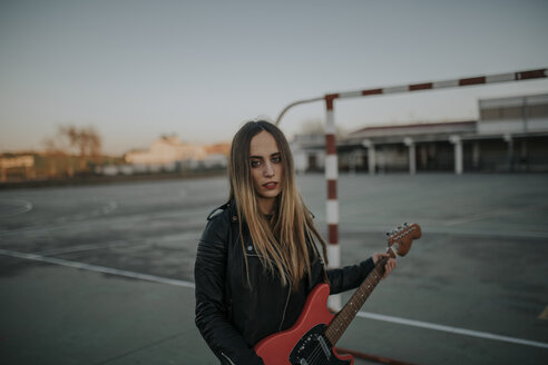 Porträt einer coolen jungen Frau mit Gitarre auf einem Sportplatz - DMGF00052