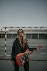 Porträt einer coolen jungen Frau mit Gitarre auf einem Sportplatz - DMGF00053