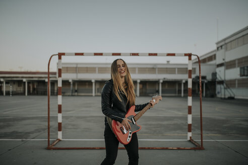 Porträt einer glücklichen jungen Frau, die auf einem Sportplatz Gitarre spielt - DMGF00054